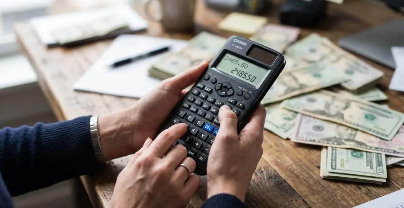 Gros plan sur des mains tenant une calculatrice avec des factures floues en arrière-plan